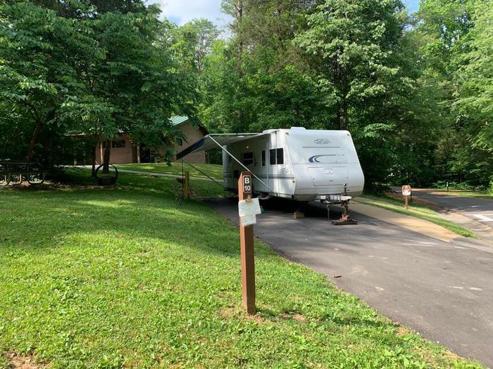 A blacktop surface with a white camper surrounded by green grass.