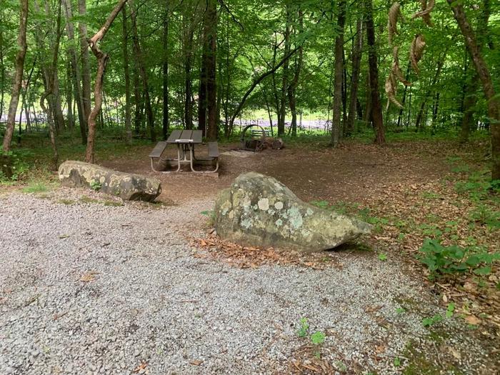 A gravel area with two gray rocks.D-20 picnic table and circle fire ring.