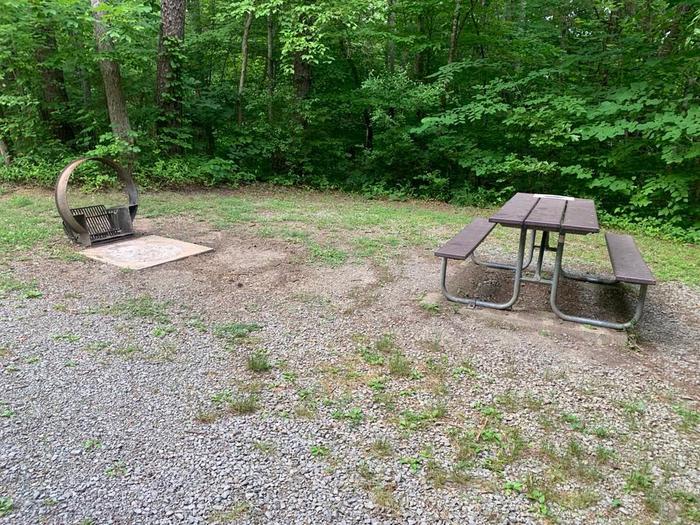 A gravel area with a brown circle fire ring and picnic table.D-22 fire ring and picnic table.