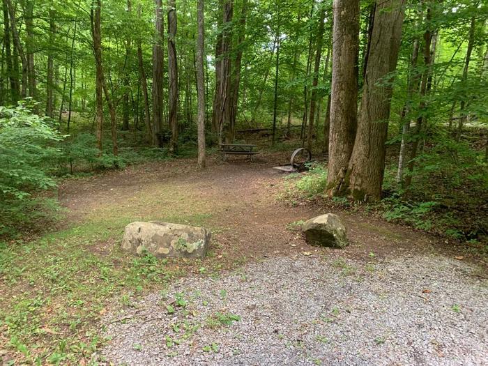 A gravel area with two gray rocks in front of a brown circle fire ring and brown picnic table.D-26 camping space.