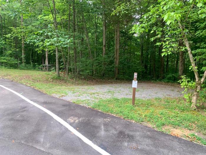 A gravel area with a small brown post near a blacktop road.D-34 camping space.