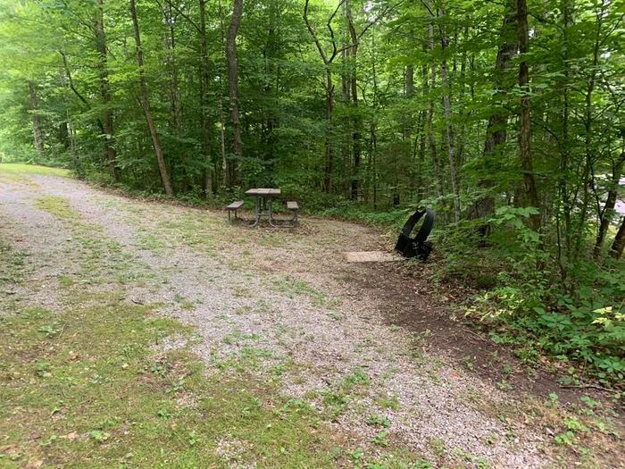 A gravel area with a brown circle fire ring and brown picnic table.E-9 camping space.