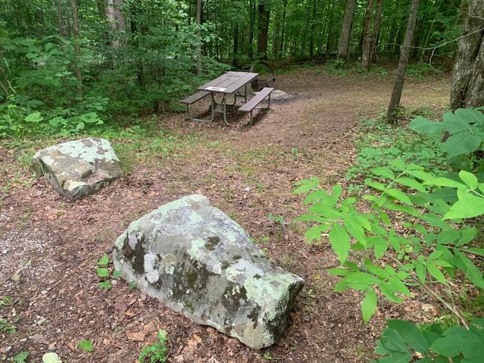 Two big gray rocks with a brown picnic table and circle fire ring.E-28 camping space.