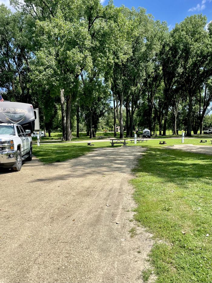 Site 2.  Electric site with grassy lawn area to one side of level driveway.  Site 2- driveway splits off from Site 1 (occupied by white truck in photo). Campfire ring located to back left of site. Lovely view of the Mississippi River.  Vault toilet restrooms and Upper Loop playground are close to the site.