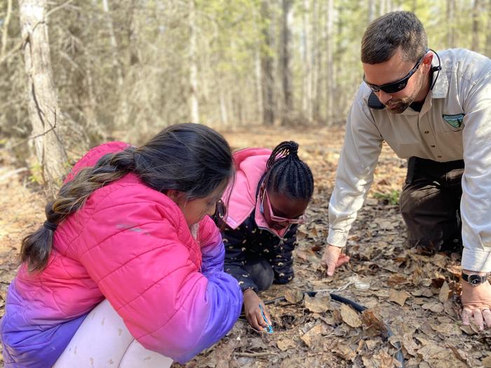Two students explore the forest floor with an instructor looking on. Forest programs help students discover the connections in the Boreal Forest!