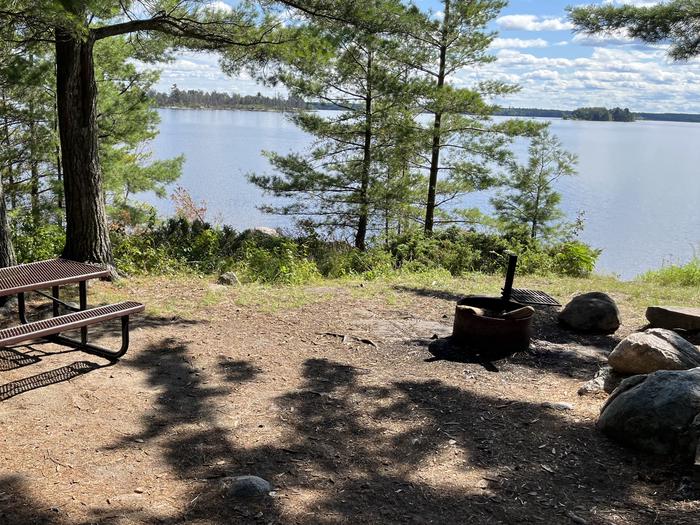 R65 - Reuter Creek, view looking out from campsite over the water with the fire ring and picnic table in the foreground.R65 - Reuter Creek campsite on Rainy Lake