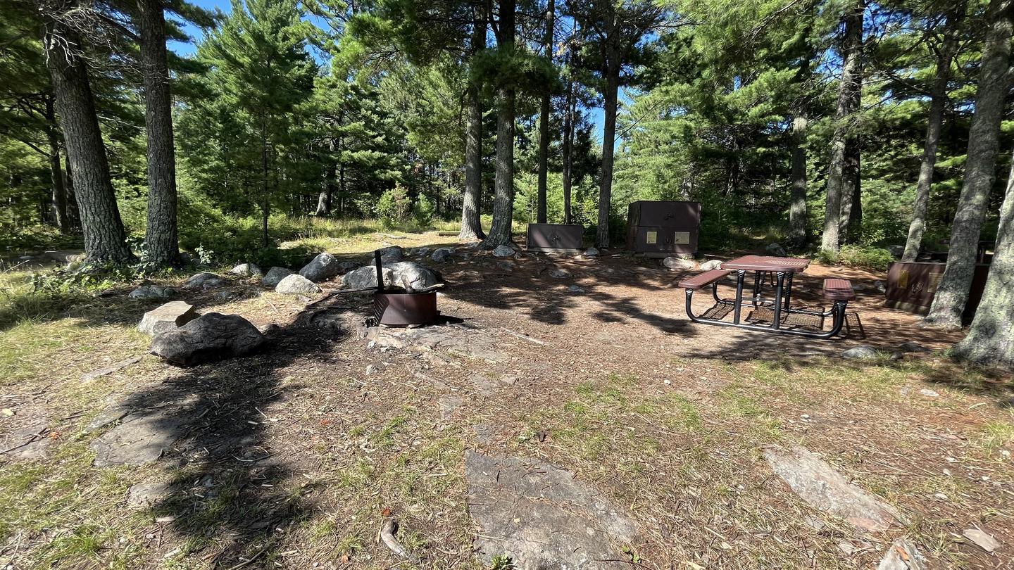 R65 - Reuter Creek, view looking into campsite core of the picnic tables, fire ring, and bear boxes with pine trees in the background.View looking into the campsite core