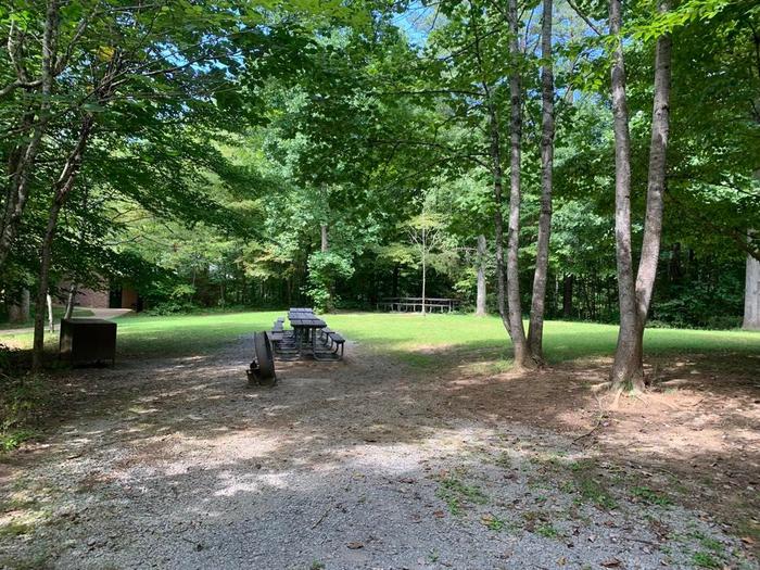 A gravel area with a brown circle fire ring and brown picnic table.G-2 camping space.