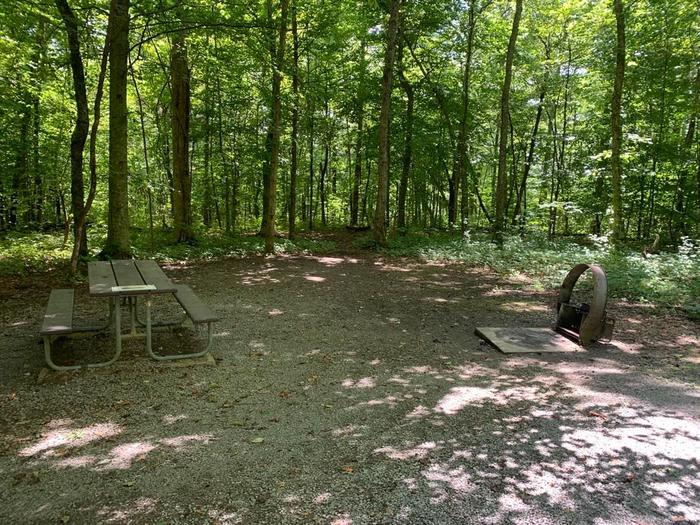 A gravel area with a circle fire ring and brown picnic table.E-2 camping space.