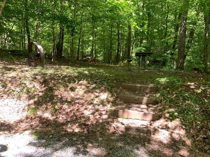 A gravel area with small brown steps heading up to the picnic table and fire ring.E-4 camping space.