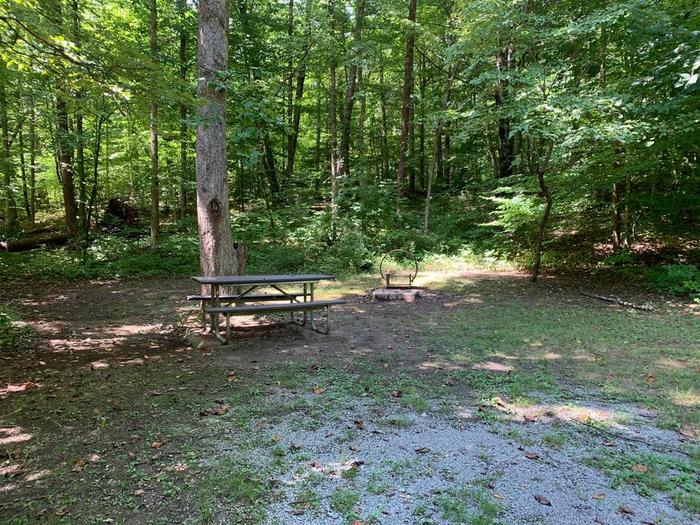 A gravel area with a brown picnic table and circle fire ring.E-10 camping space.