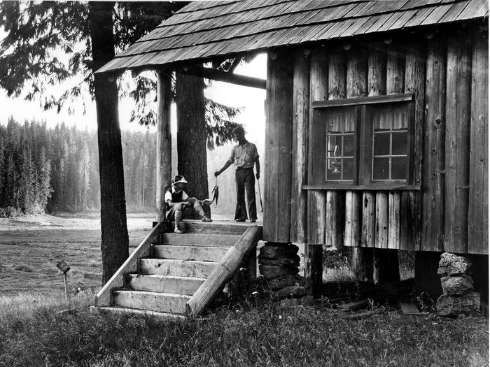 A black and white historic photo of two kids holding fish on the porch of Hall House CabinHall House Cabin