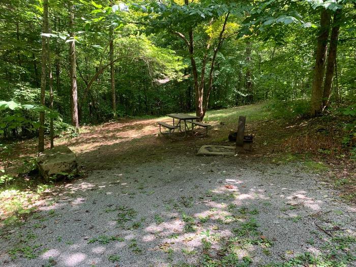 A gravel area with a circle fire ring and brown picnic table.E-27 camping space.