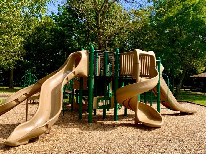 Playground with 4 tan slides and green climbing poles. Playground shared between Beech and Dogwood Picnic Shelter