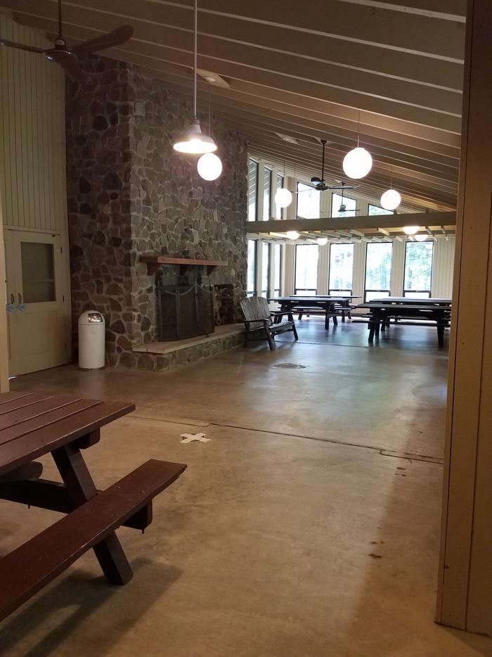 Inside of Clark Lake pavilion showing room layout with fireplace, windows, benches, and picnic tables.Inside of the Clark Lake pavilion from the north end of the room.