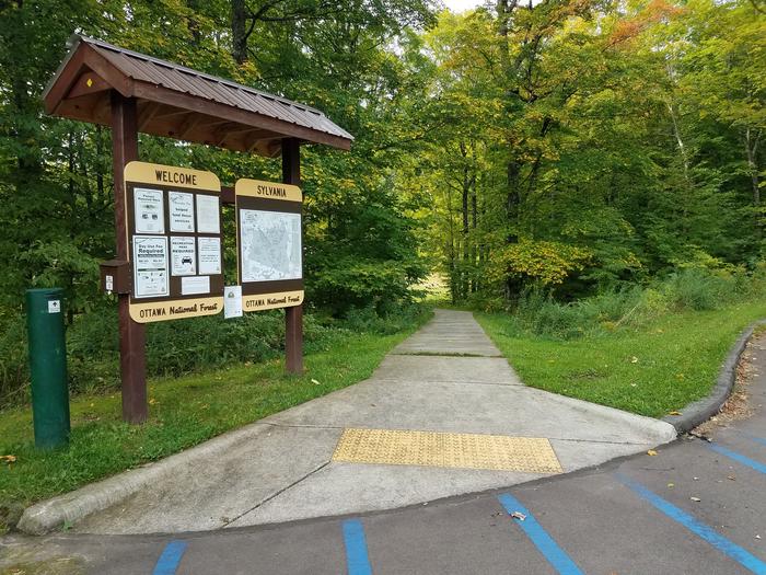 Fee tube, bulletin board, and accessible path to the Clark Lake pavilion from the parking area.Path from the parking lot to the Clark Lake pavilion.