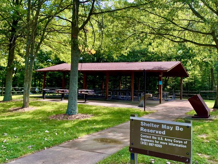 Brown wooden shelter surrounded by mature trees and green grassDogwood Picnic Shelter view from walking path