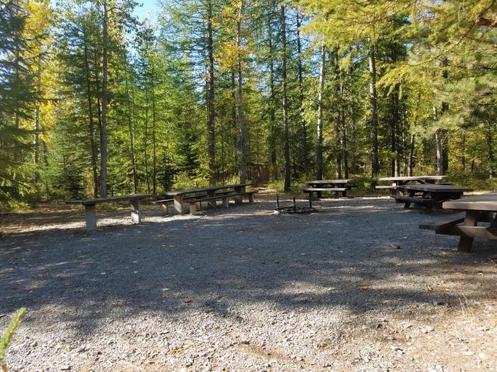 A photo of Site 001 of center gathering area with 4 moveable tables, 1 16’ permanent table by a 10’ prep table (no benches) AREA BIG CREEK CAMPGROUND at Big Creek Campground (Flathead National Forest, MT) with Picnic Table, Fire Pit, Shade, Tent Pad, Waterfront