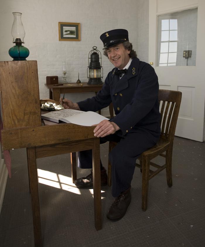 A man dressed as a lighthouse keeper sits at a desk.Historic Yaquina Head Lighthouse tours.
