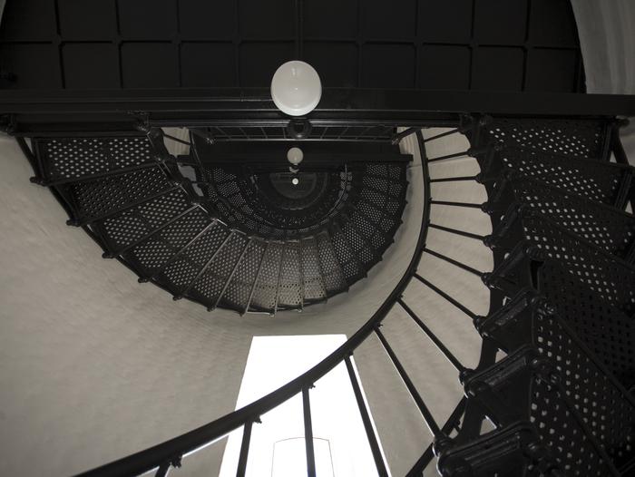 White walls, a window, and a black cast iron spiral staircase.Spiral staircase to the Watch Room.
