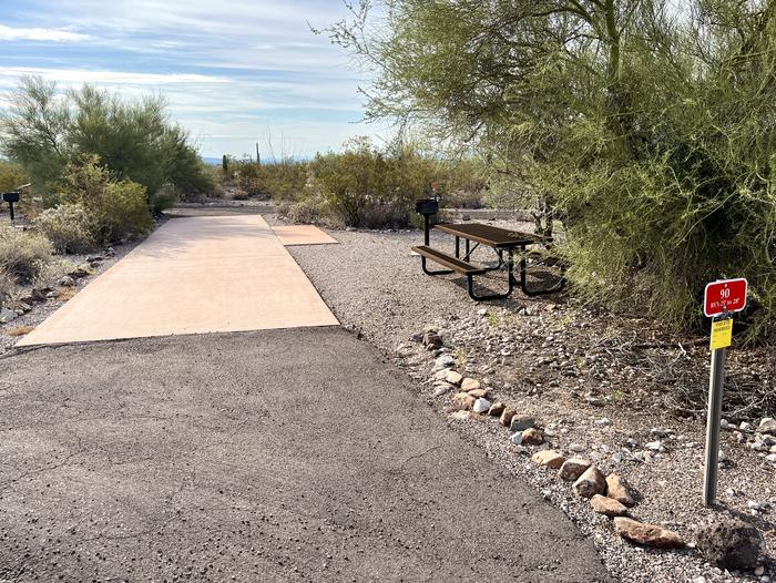 The driveway of the site with the picnic table and grill surrounded by desert plantsEach campsite is marked by a placard to easily identify which site it is.