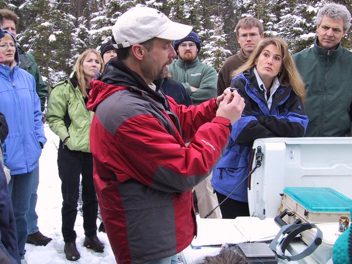 A biologist holding a small songbird discusses the process of bird banding to onlookers.Public Programs provide the opportunity to learn directly from scientists about their work.