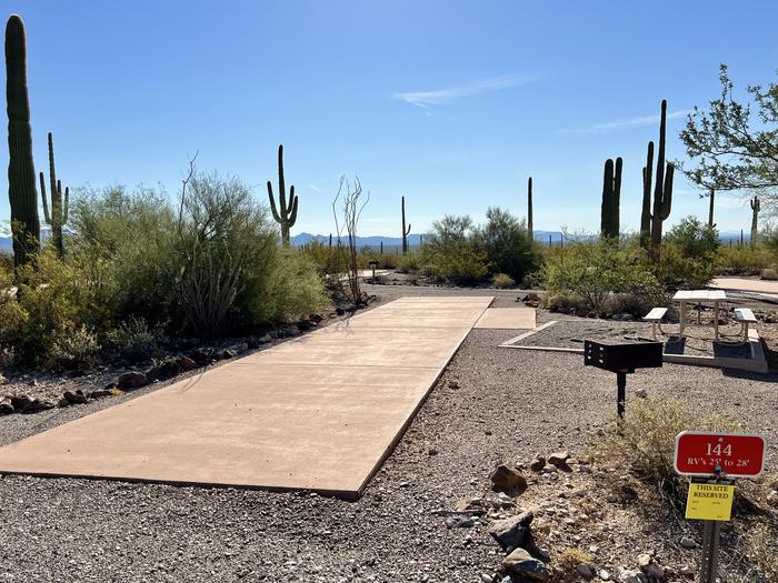 Pull-thru campsite with picnic table, tent pad, and grill, surrounded by cactus and desert vegetation.The entrance into Site 144