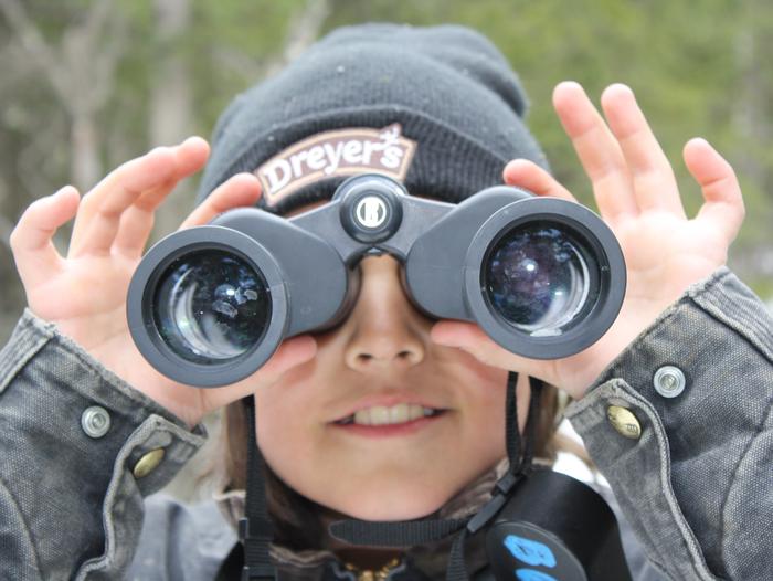 Kid with binoculars looking directly at the camera.A young program participant looking with binoculars.