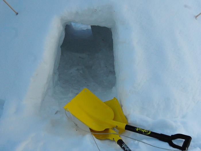 Entrance to a snow shelter with avalanche shovelsShovels lie in the snow outside the entrance to a quinzhee  snow shelter that is being dug out.