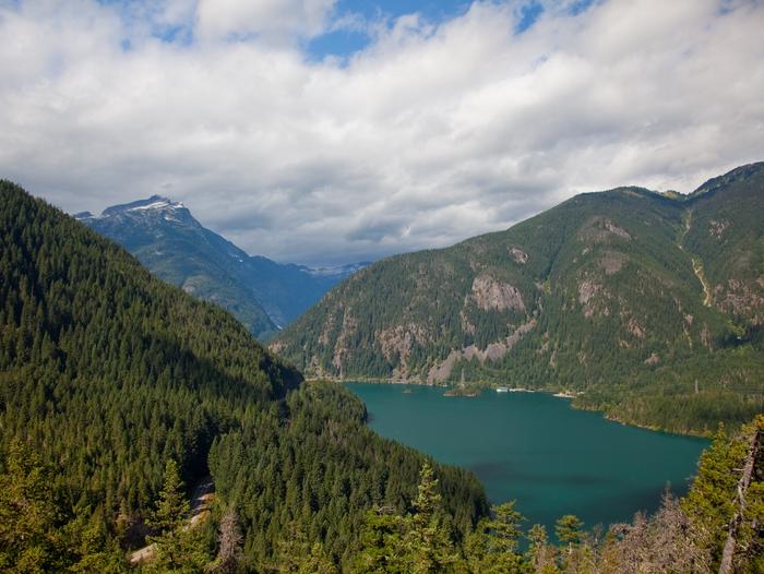 A view of Diablo Lake, surrounded by forested mountains and blue sky with clouds.Hike the nearby Thunder Knob Trail for views of Diablo Lake.