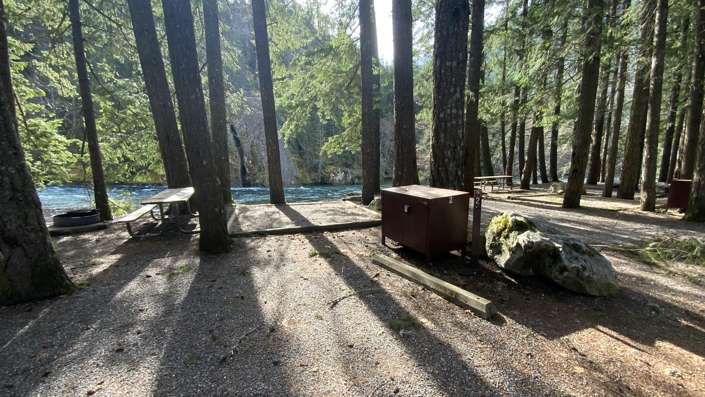 Sunny campsite near the lake containing a bear box, picnic table, and campfire ring.Lakeside campsite.