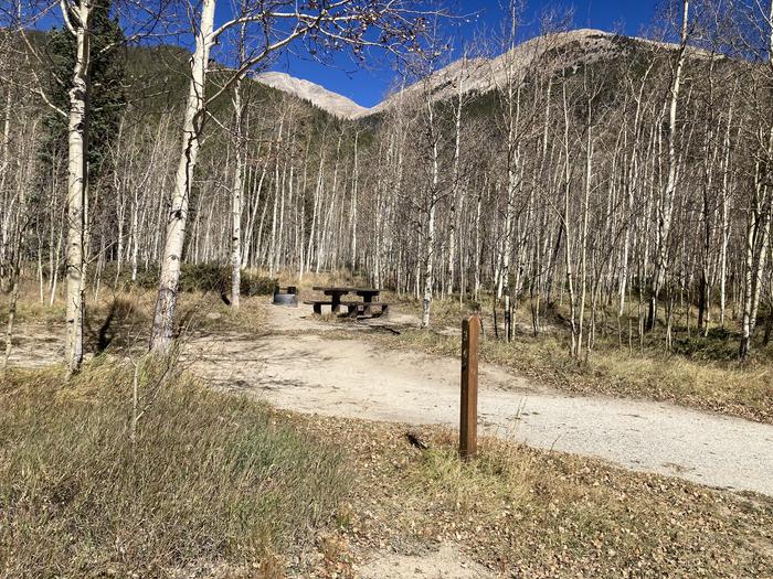 Dirt parking area with picnic table, trees and mountains in background.A photo of Site 034 parking area with site post.