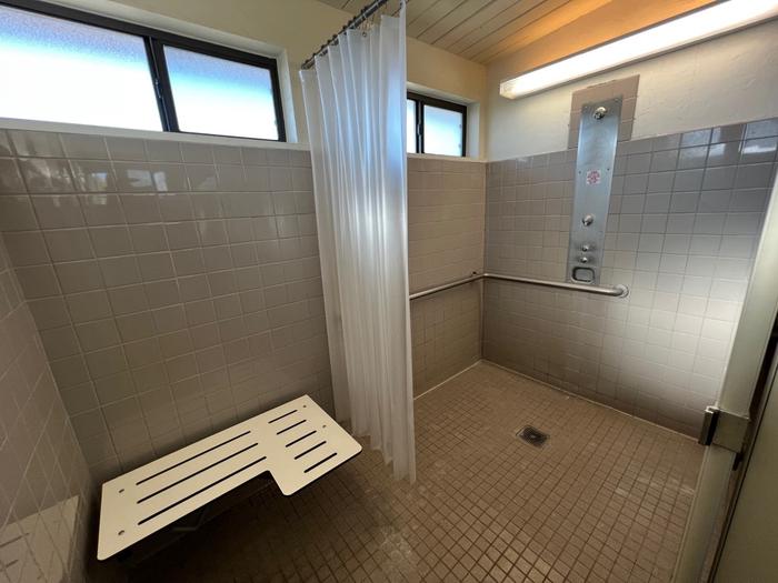 An ADA accessible shower stall with handrails, shower curtain, and a seat.One of the free solar-heated showers.