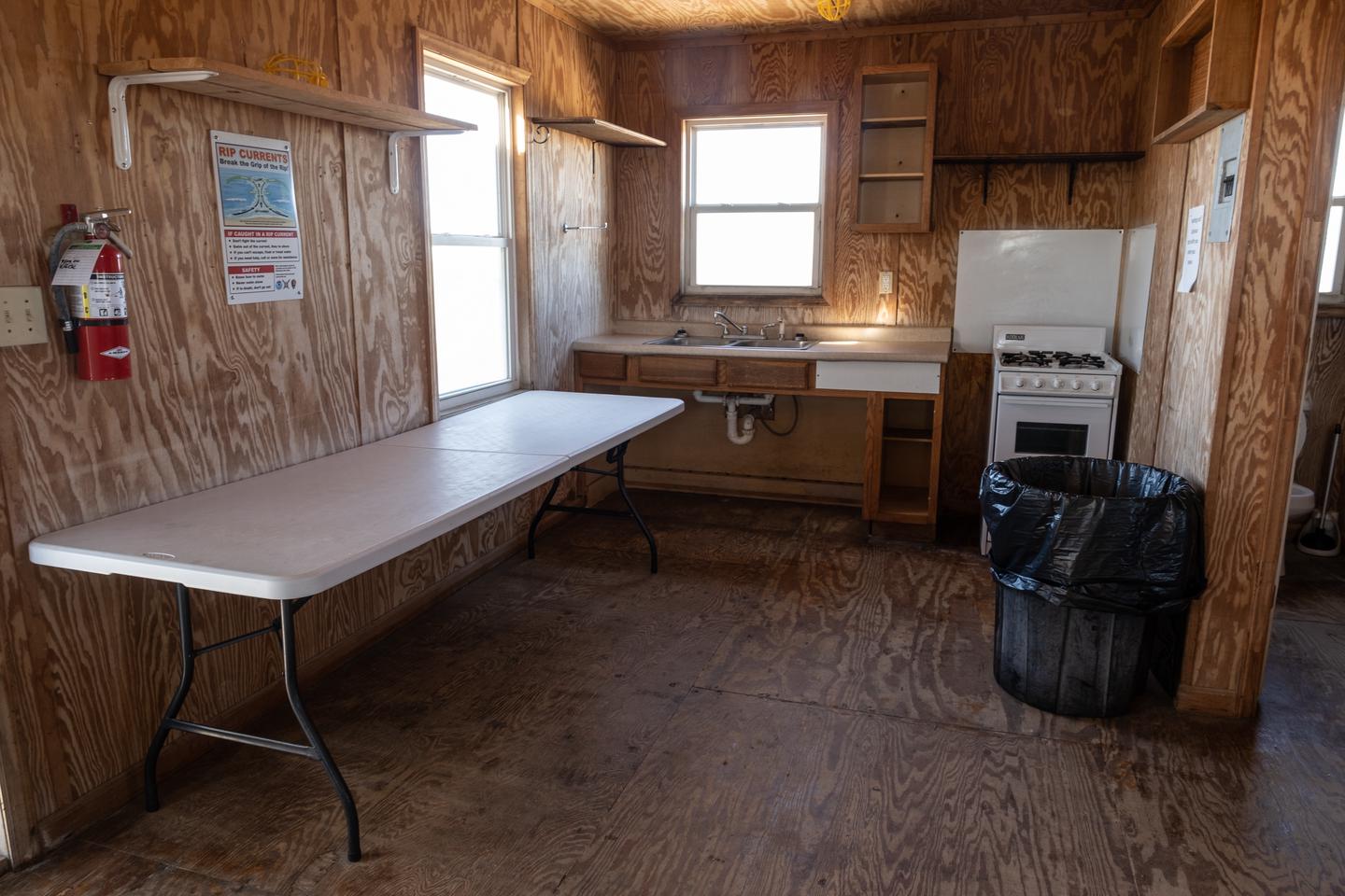 A view of the kitchen area, showing a table, sink, countertop, and propane range, as well as the bathroom doorway to the right.Kitchen area.