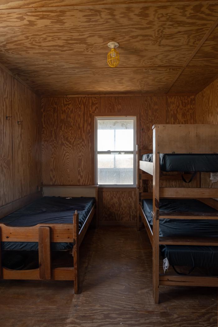 A view of the second bedroom, with 1 bunk bed along the right wall, and 1 single bed along the left wall. The remaining 3 beds are out of frame.Bedroom 2, with 3 of the 12 total beds, and the remaining 3 behind the camera.
