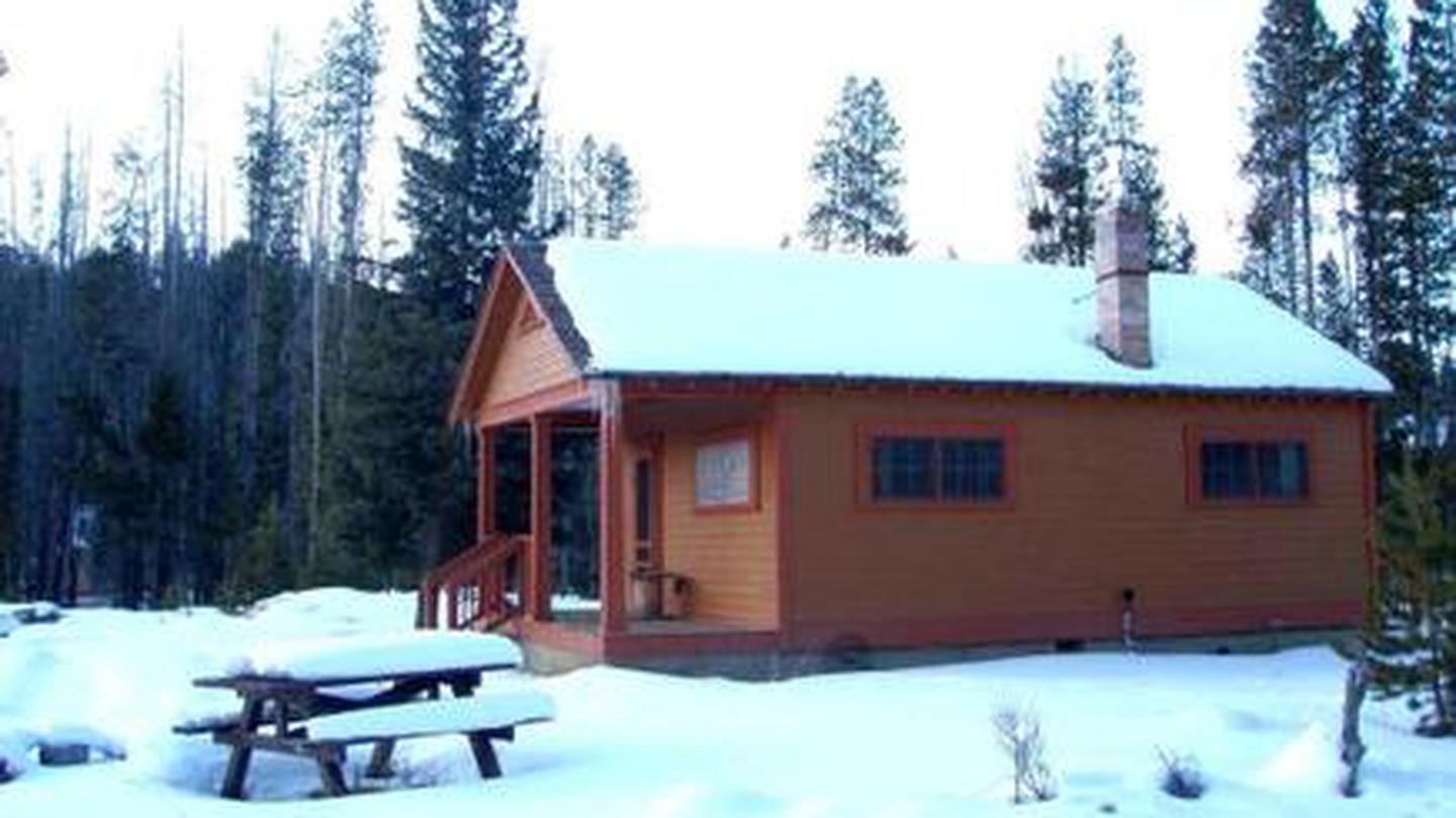 Thick snow covers a wooden cabin and picnic table.Redfish Cabin