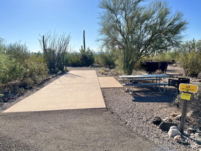 Pull-thru campsite with picnic table and grill, cactus and desert vegetation surround site.  The entrance into Site 069