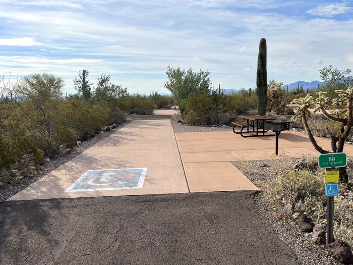 Pull-thru campsite with picnic table and grill, cactus and desert vegetation surround site.  Handicap logo painted on the groundThe entrance into Site 088