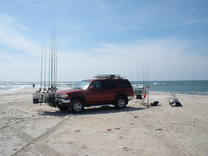 4Runner SUV, with fishing rods attached to front and back of vehicle, on beach sand in foreground and water in background 4Runner SUV parked on beach