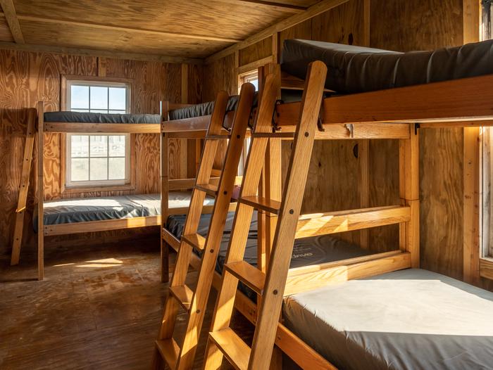 Sunlight shining on 3 bunk beds in a plywood cabinA view of the bedroom area in one of the cabins