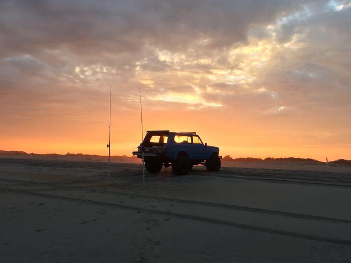 Jeep with casting rods on the beach backlit by the sunrise.Surf fishing and sunrise...a hard combination to beat!