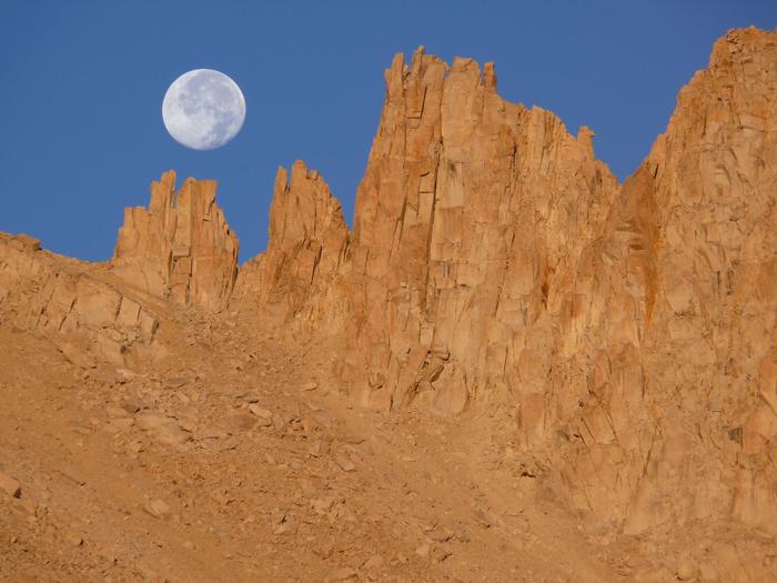 Full moon sets over pinnacles of the Sierra Crest.Dawn light illuminates the Sierra Crest as a full moon sets.