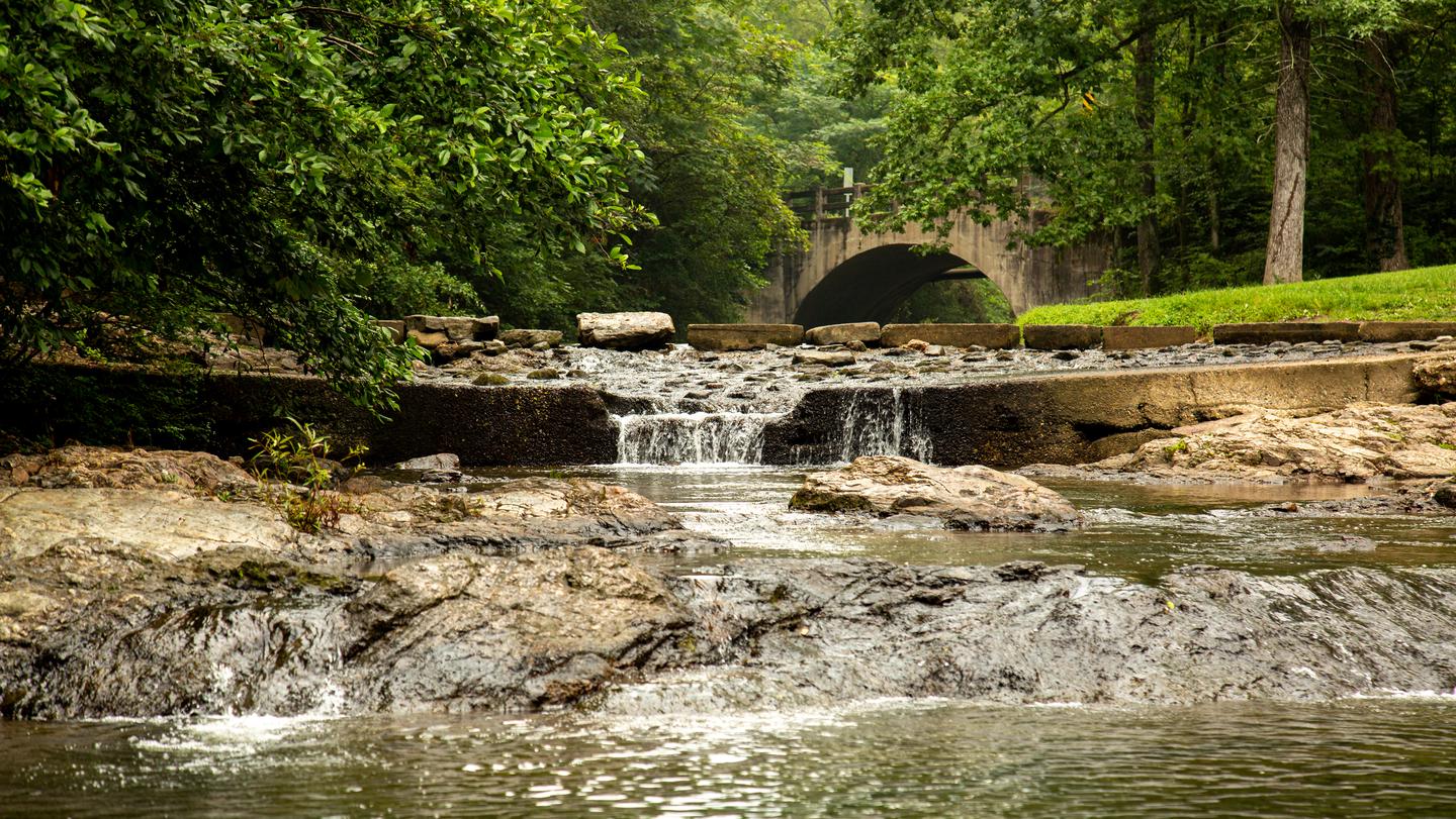 Gulpha Gorge Creek runs over boulders surrounded by trees with a quaint bridge in the backgroundGulpha Gorge Creek runs alongside the campground.