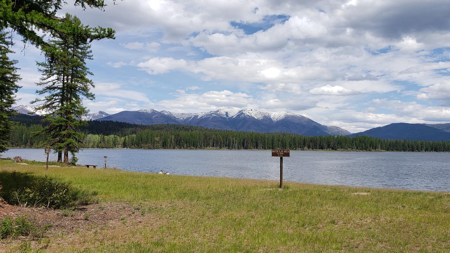 View from swim beach at Seeley Lake Campground, looking east across Seeley Lake. Snow-capped peaks of the Swan Range can be seen in the background. View from swim beach at Seeley Lake Campground.