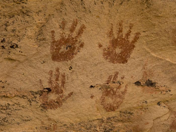 A yellow sandstone wall with four red handprints, one left-right pair on top of the other.