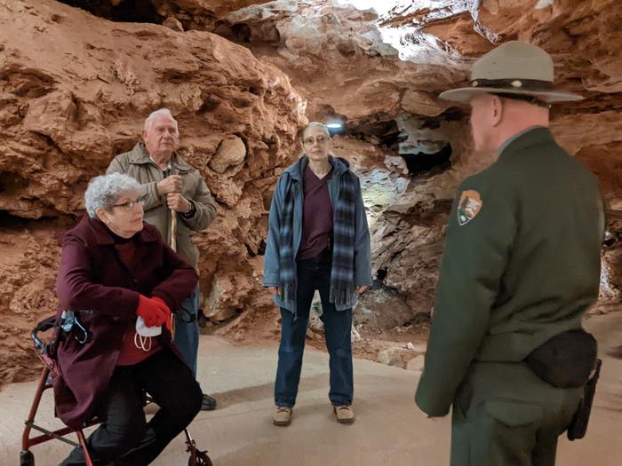 A ranger and three visitors, one sitting on a walker, in a room of a cave.The 30-minute Accessibility Tour encounters no stairs.