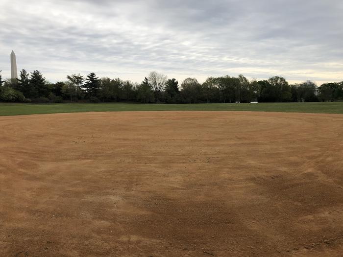 A view of field S4 from the infield. Beyond the infield, a grassy outfield is bordered by trees with views of the Washington Monument and Thomas Jefferson Memorial.Field S4 as seen from the infield.