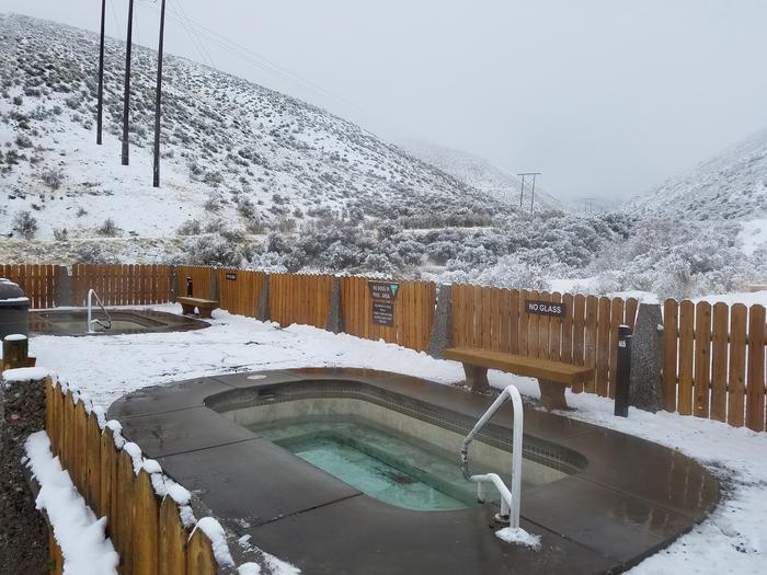 View of two small concrete pools at Sharkey Hot Springs in winter with snow on adjacent hillsides.View of Sharkey Hot Springs pool in winter with snow.