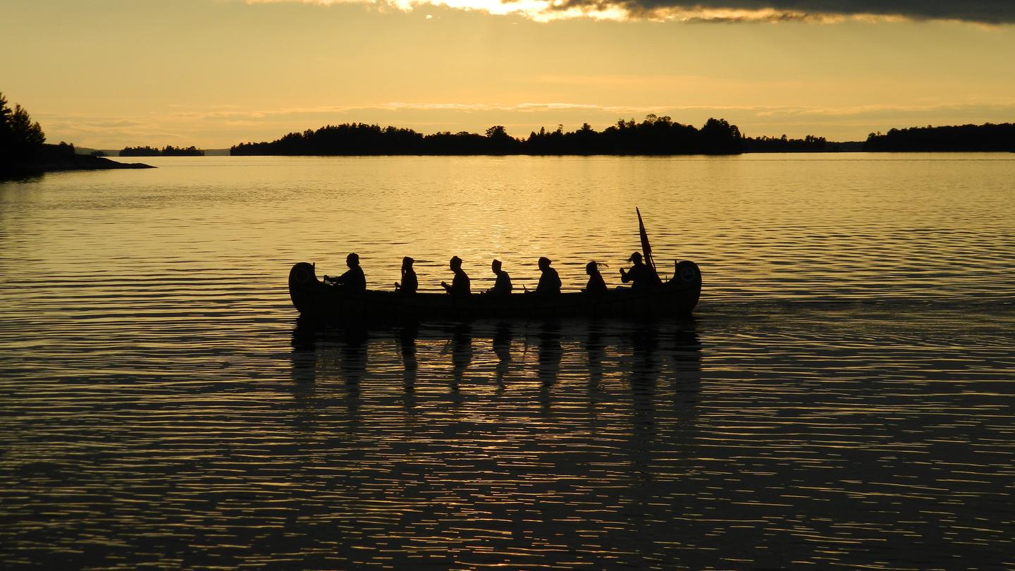 Park visitors paddle a large canoe on a calm lake.Park visitors paddling a 26-foot north canoe.
