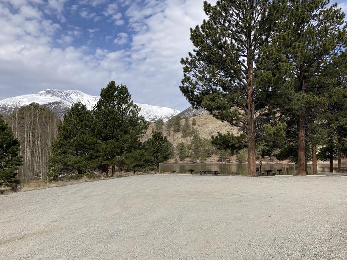 Gravel parking area next to lake with snow covered mountain in background.